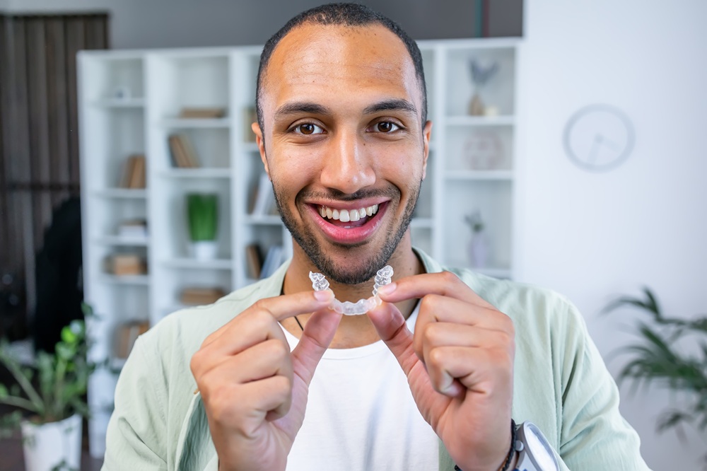 A cheerful man holds up his Invisalign clear aligners at home, demonstrating the ease and confidence that come with modern orthodontic care - invisalign naples fl