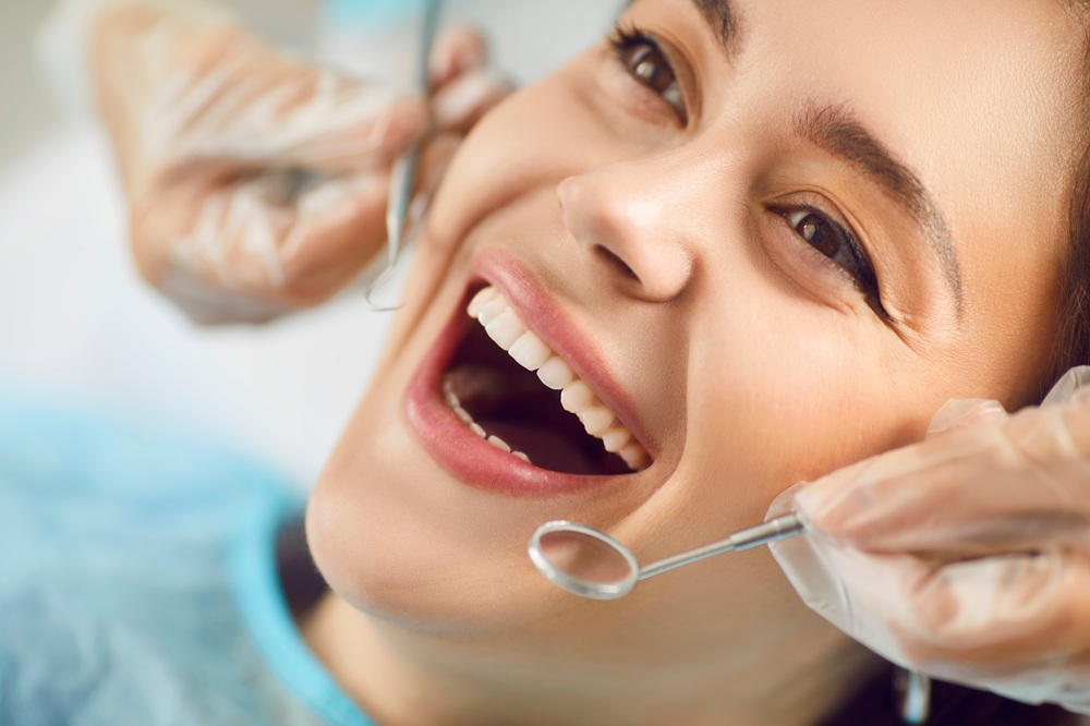 A smiling woman undergoes a dental examination as a dentist uses a mirror and probe to check her teeth during a routine checkup - are cavities contagious