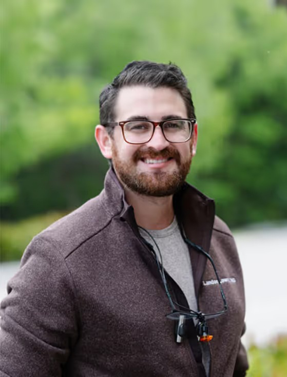 Dr. Landon Smiling Outdoors – Dentist in Naples, FL Portrait of Dr. Landon standing outside, smiling warmly while wearing glasses and a casual jacket, showcasing his friendly and approachable demeanor – Dentist in Naples, FL
