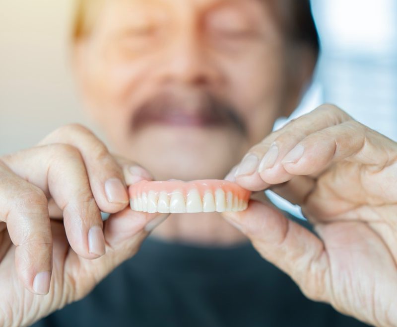 An elderly man carefully holds a set of dentures in his hands, illustrating the importance of proper care and repair for broken or damaged dentures - denture repair near me