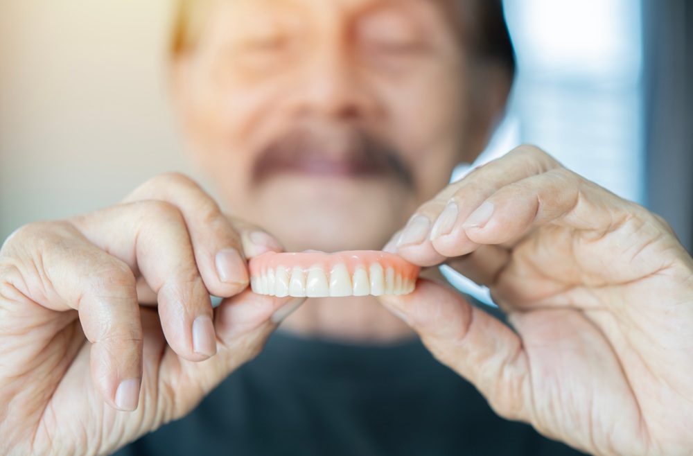 An elderly man carefully holds a set of dentures in his hands, illustrating the importance of proper care and repair for broken or damaged dentures - denture repair near me