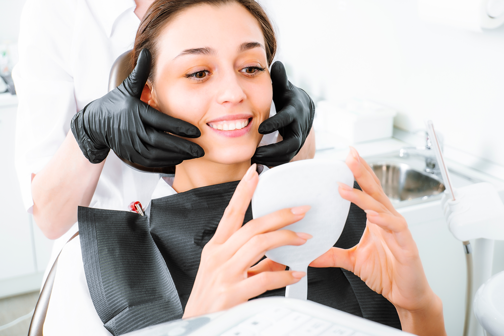 A woman at the dental clinic admires her reflection in a mirror while her dentist adjusts her aligners, highlighting the satisfaction of Invisalign results - invisalign naples fl