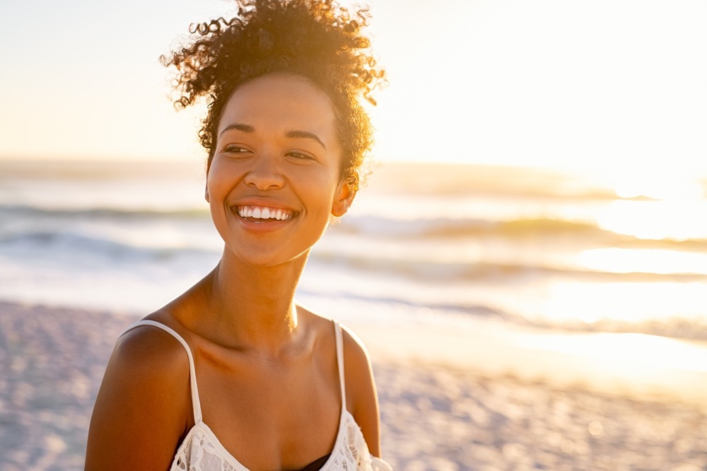 Confident Smile by the Beach – Suncoast Dental Center - suncoast dental center reviews A woman with a radiant smile enjoys the sunshine on the beach, symbolizing confidence and happiness after achieving a healthy smile with Suncoast Dental Center - suncoast dental center reviews